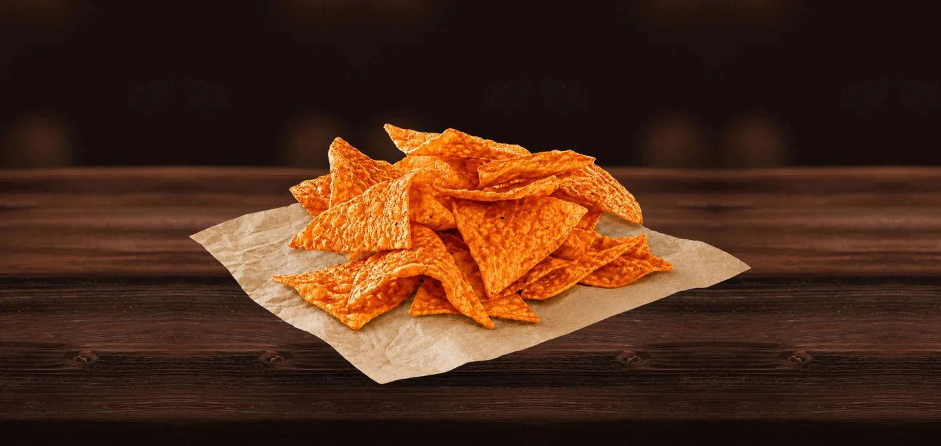 Pile of orange tortilla chips on a sheet of brown parchment paper atop a dark wooden table.