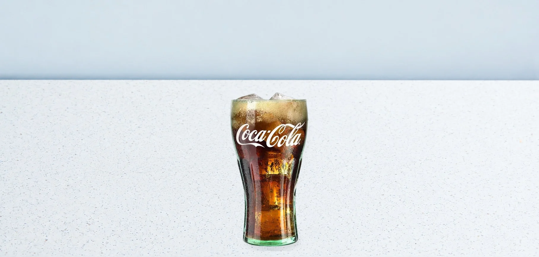 2980-coca-cola-04 | Taco Bell Hrvatska Glass of Coca-Cola with ice on a speckled white counter against a pale blue background