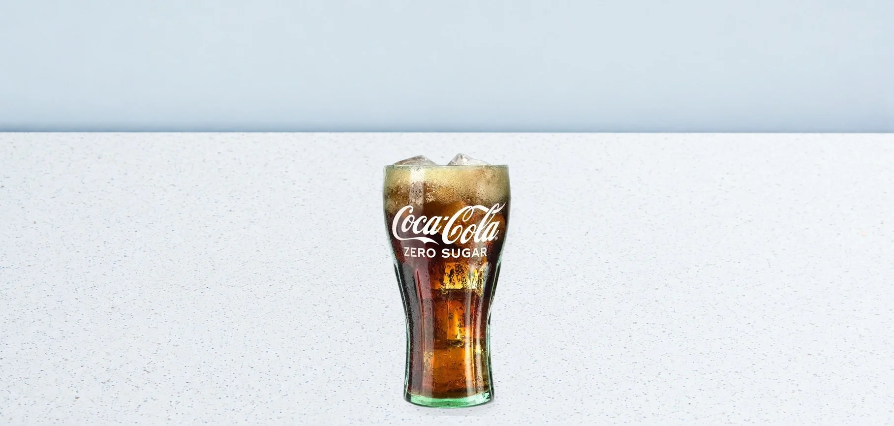 2981-coca-cola-zero-04 | Taco Bell Hrvatska Tall Coca‑Cola glass with ice on a speckled white counter, labeled Coca‑Cola Zero Sugar.