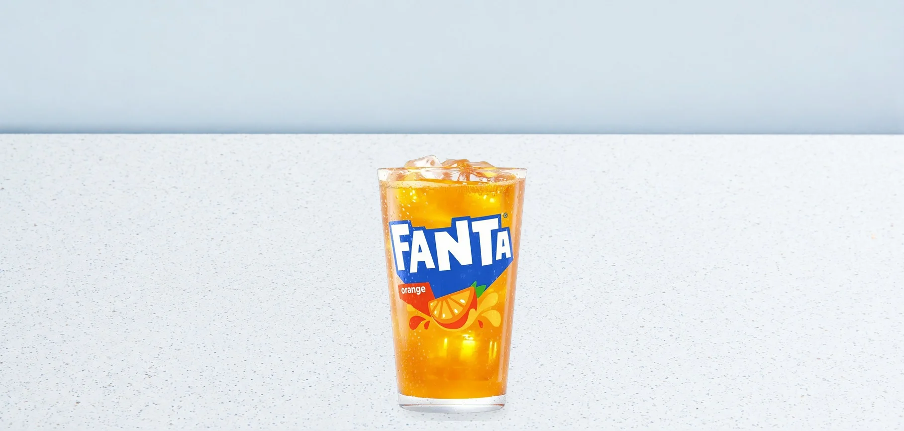 2982-fanta-04 | Taco Bell Hrvatska Glass of orange Fanta with ice on a white speckled counter against a pale blue background, centered image